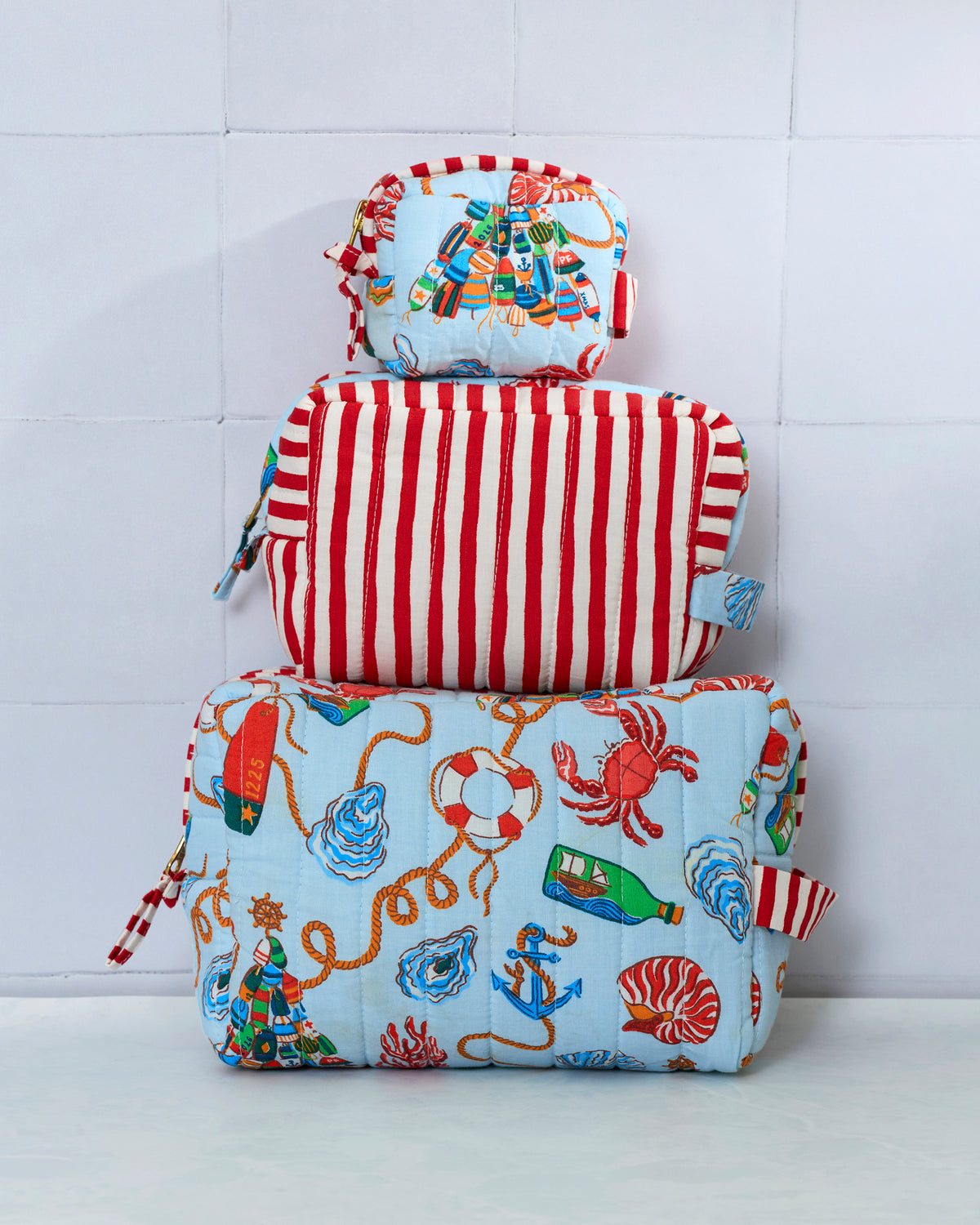 Three pouches stacked vertically, showing a pale blue nautical print and a red-and-white striped pouch.