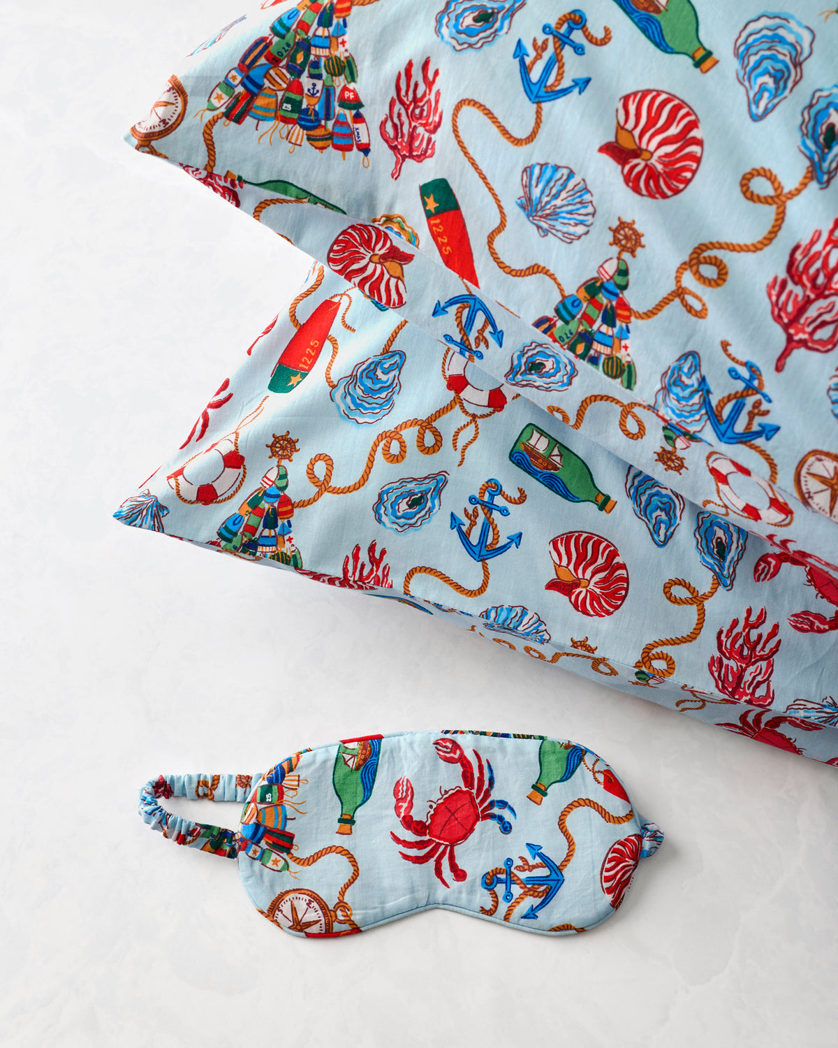 Two pillowcases and a matching eye mask in a light blue nautical print with anchors, shells, ropes, and sea creatures.