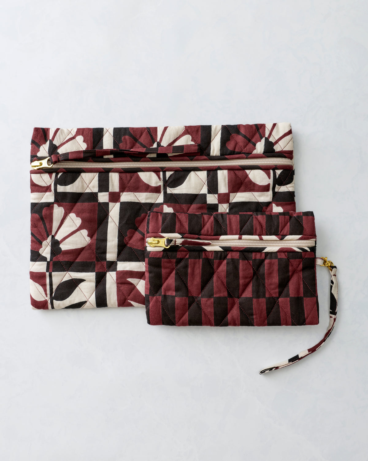 Two quilted zippered pouches in burgundy, cream, and black floral and geometric prints shown together.