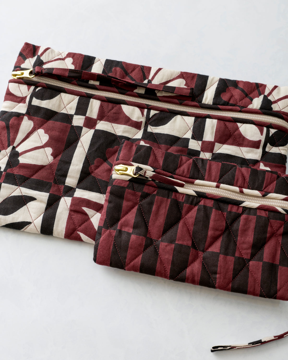 Close view of two quilted zippered pouches with burgundy, cream, and black floral and geometric prints.