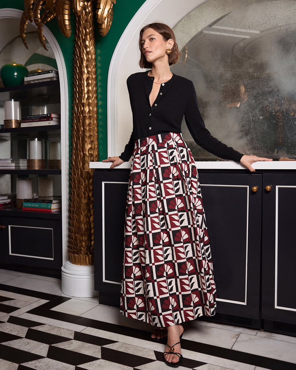 Full-length view of a model wearing the Bordeaux Sparrow Skirt with its geometric floral print, paired with a black cardigan and black strappy sandals.