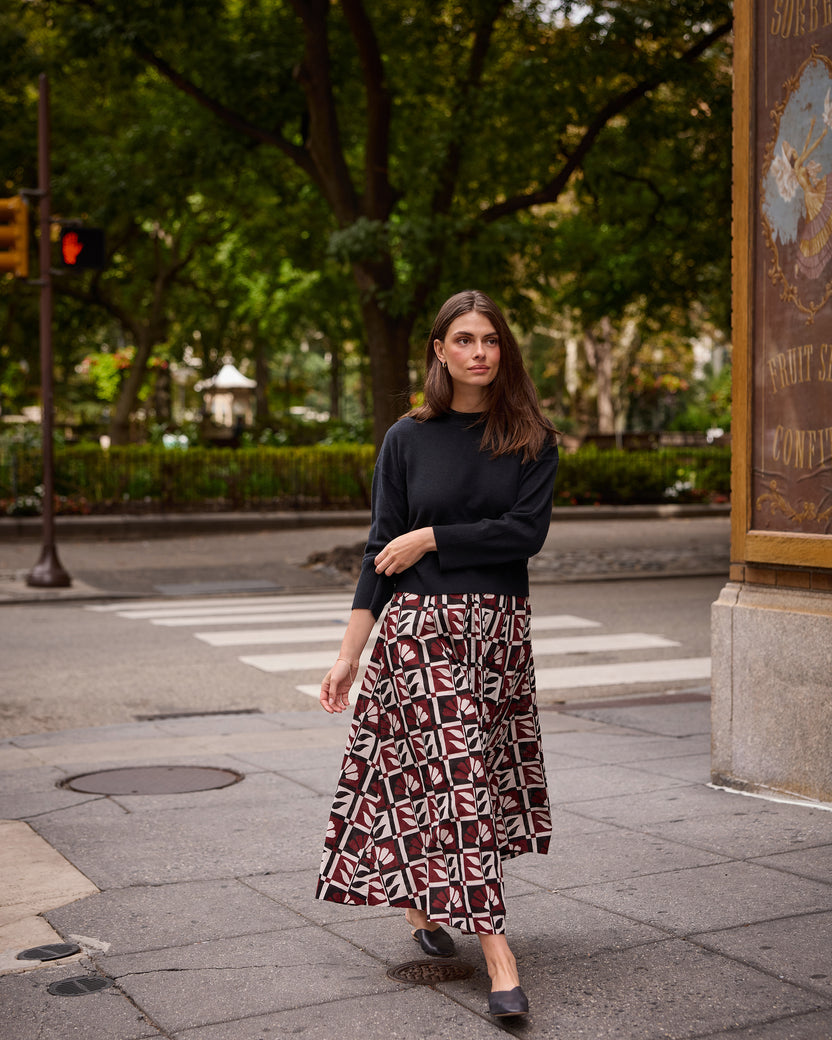 Full-length outdoor view of a model wearing the Bordeaux Sparrow Skirt with a black long-sleeve top and black flats.