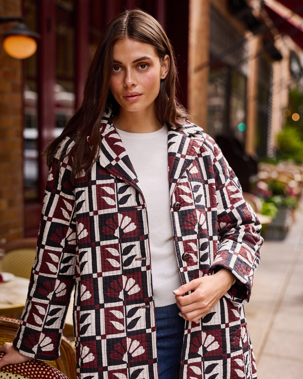Person standing outside a café wearing a burgundy, cream, and black geometric-patterned Spencer jacket over a white top.