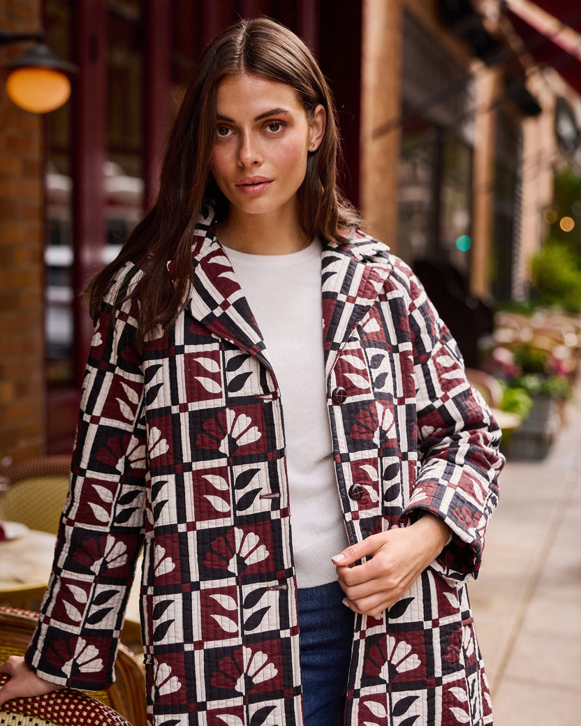 Person standing outside a café wearing a burgundy, cream, and black geometric-patterned Spencer jacket over a white top.