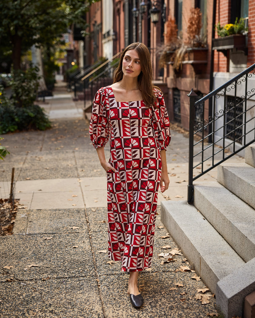 Person walking on a residential sidewalk wearing a red-and-cream geometric-patterned Constance dress with puff sleeves.