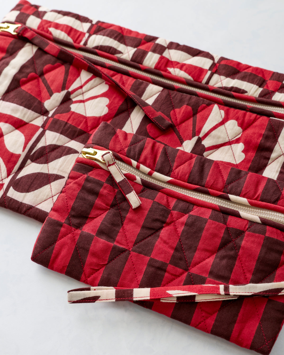 Close-up of two quilted zippered pouches in the Poppy print, showing the floral pattern, stitching, zippers, and wrist strap.