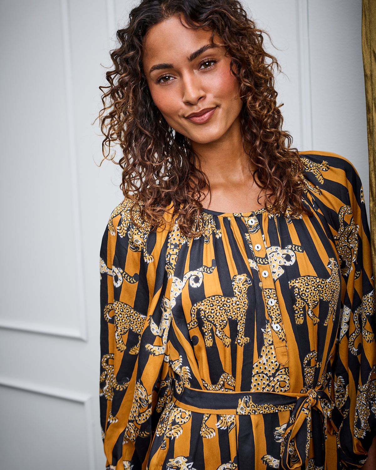 Close front view of the Leopard Stripes Felicity dress on a model, showing the gathered neckline, button placket, waist tie, and mustard-and-black leopard stripe print.