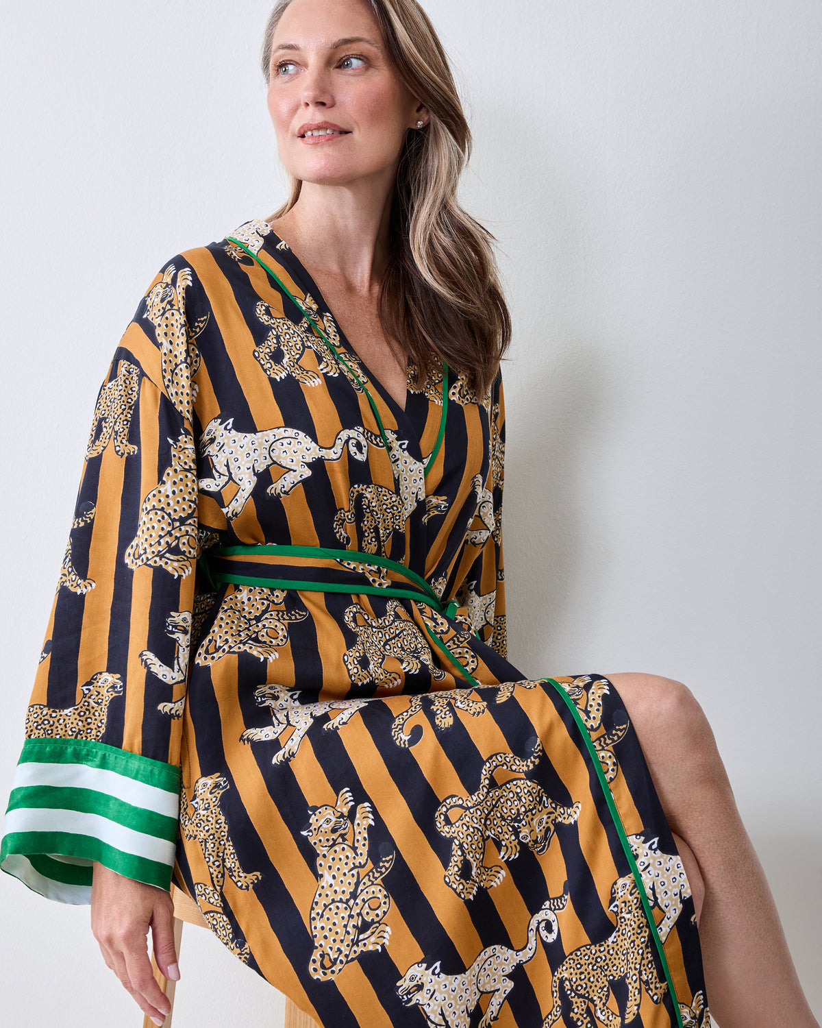 Seated view of a butterscotch-and-black striped robe with leopard illustrations, green trim, contrasting striped cuffs, and a matching belt.