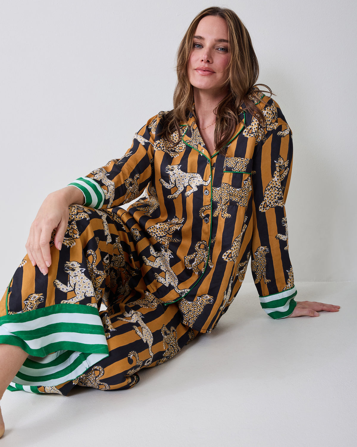 Person seated in the Leopard Stripes Soho set in butterscotch, with a long-sleeve button-front top and wide-leg pants featuring leopard prints and green-and-white trim.