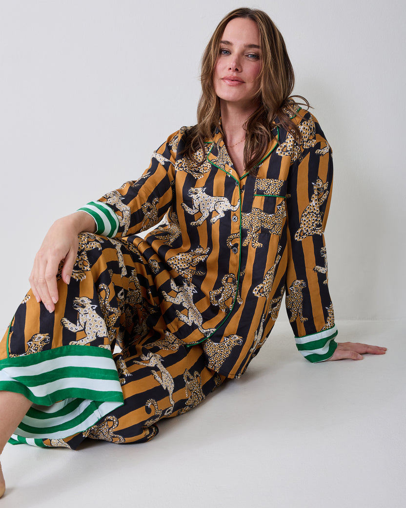 Person seated in the Leopard Stripes Soho set in butterscotch, with a long-sleeve button-front top and wide-leg pants featuring leopard prints and green-and-white trim.