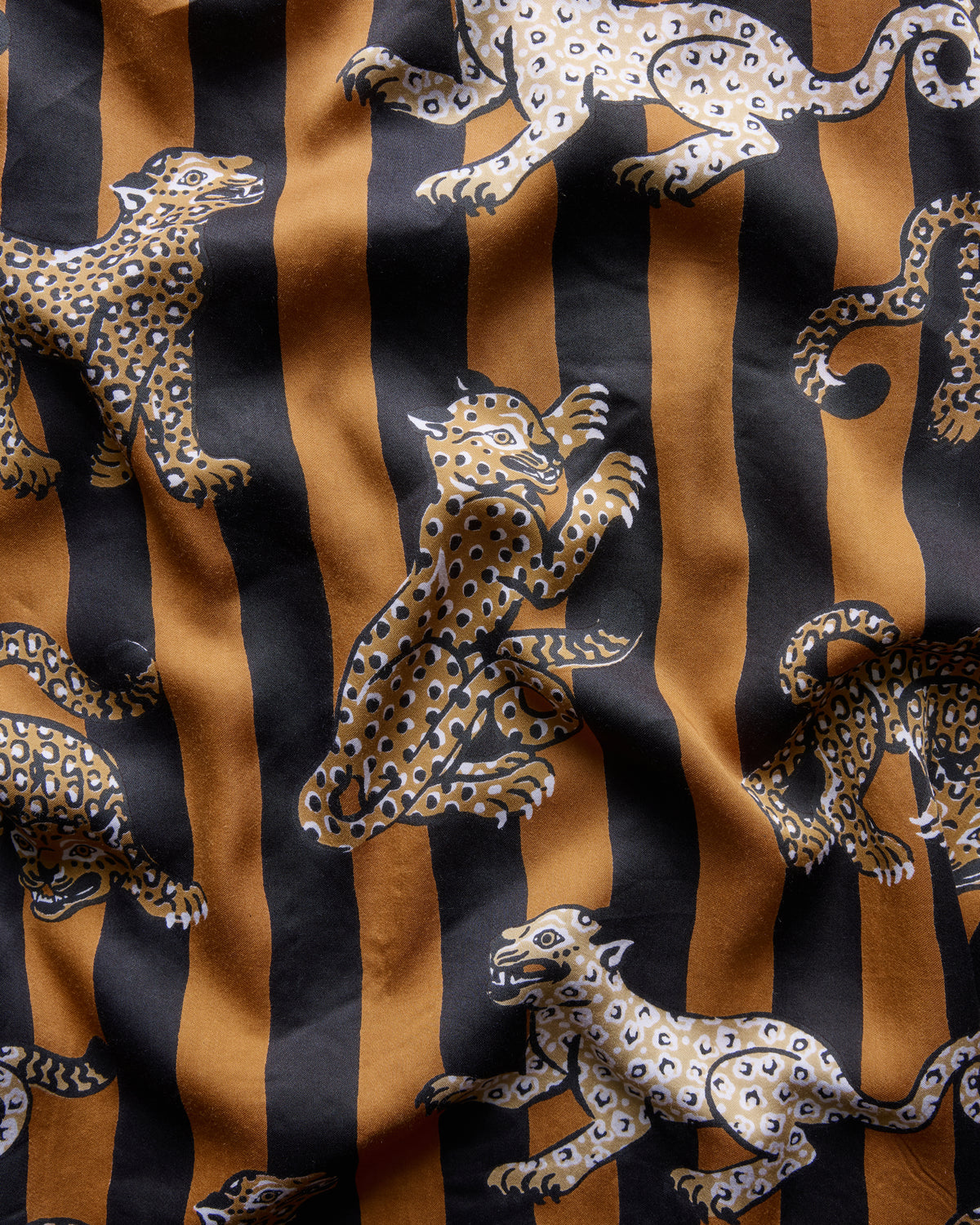 Close-up fabric detail showing repeated leopard motifs over alternating mustard and black vertical stripes.