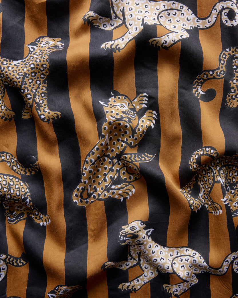 Close-up fabric detail showing repeated leopard motifs over alternating mustard and black vertical stripes.