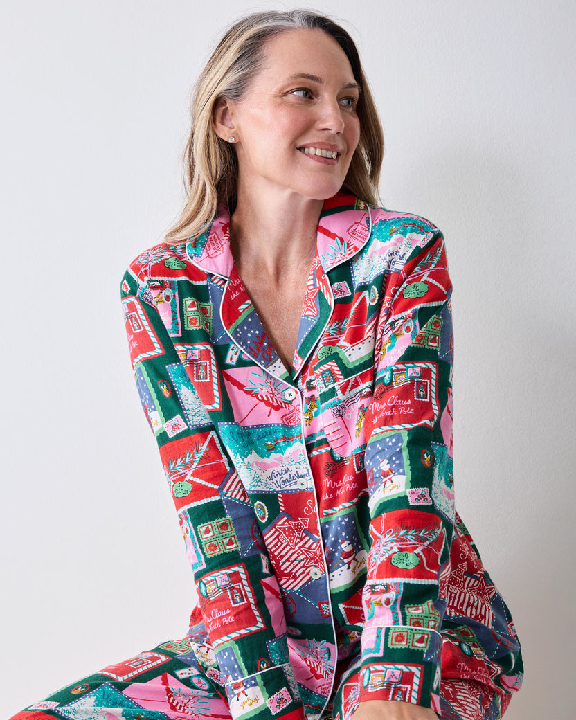 Three-quarter view of a model wearing a long-sleeve button-front pajama top and matching pants with a colorful Christmas postcard print.