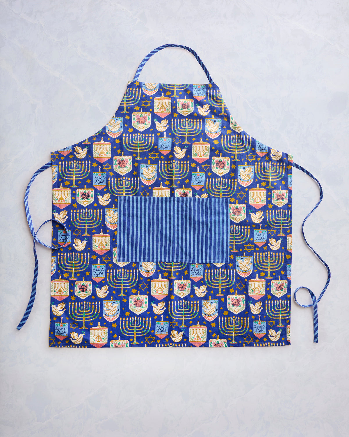 Flat view of a blue patterned apron with menorahs, stars, birds, and a large striped front pocket.