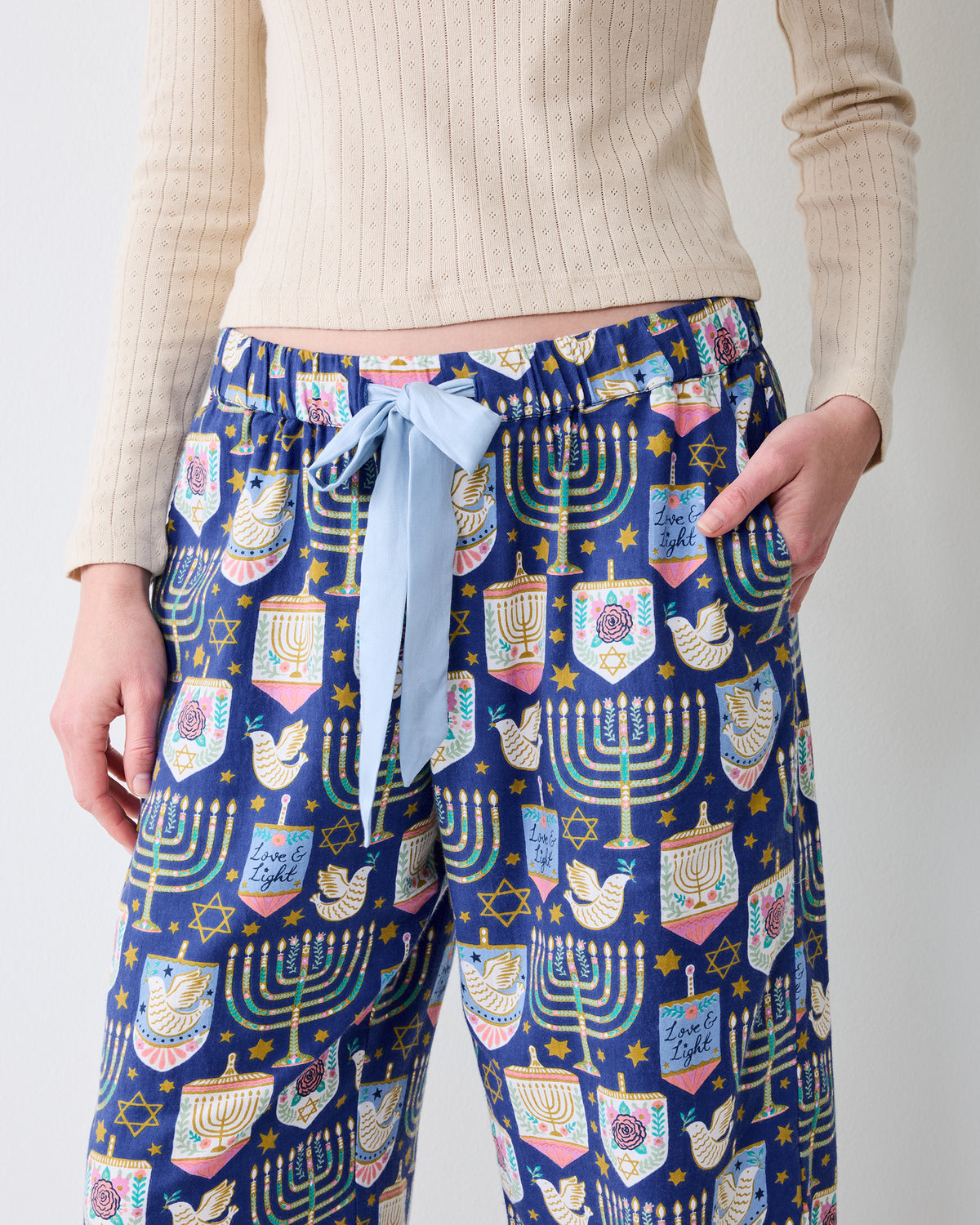 Front detail of Hanukkah Blue Astrid pajama pants showing the drawstring waist, side pockets, wide legs, and repeating menorah and holiday print.