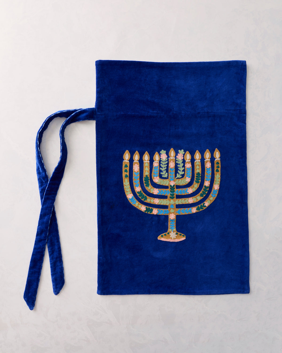 Flat view of a blue gift sack with an embroidered gold-and-pink seven-branched menorah and two ties.