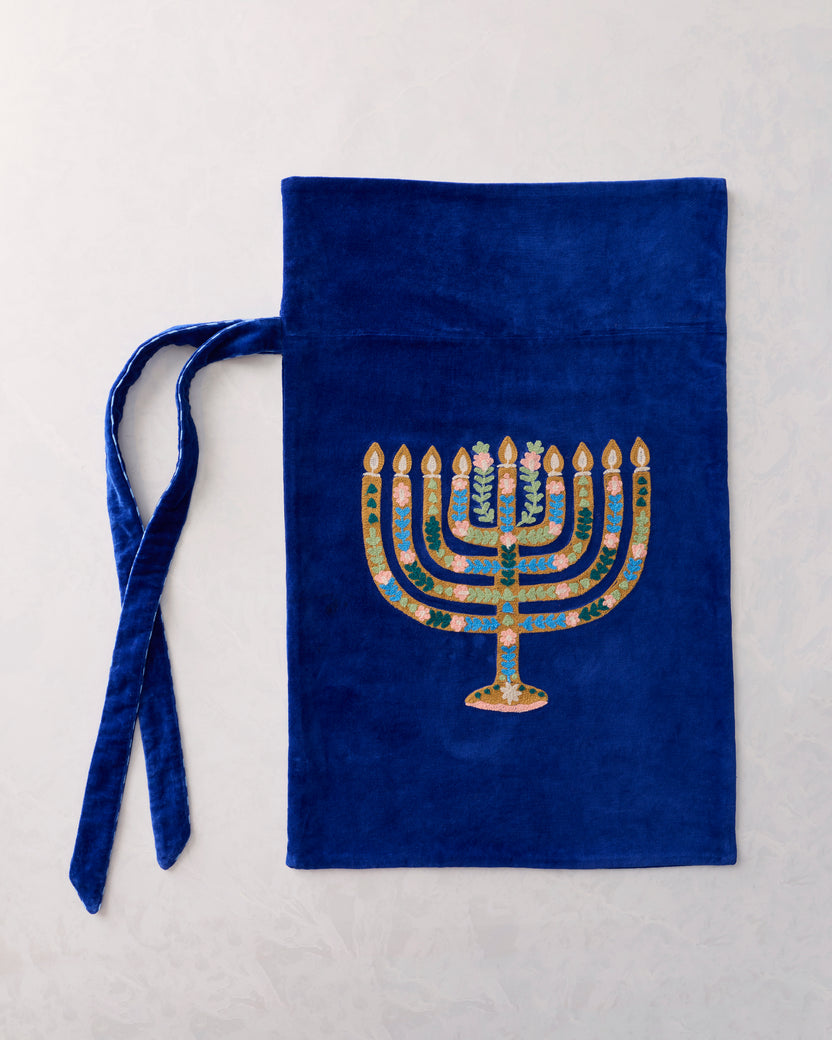 Flat view of a blue gift sack with an embroidered gold-and-pink seven-branched menorah and two ties.