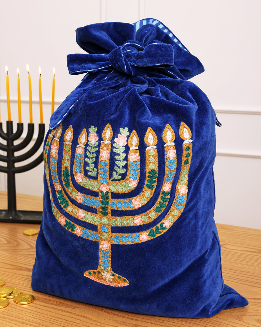 Blue embroidered gift sack with a Hanukkah menorah design, tied at the top.