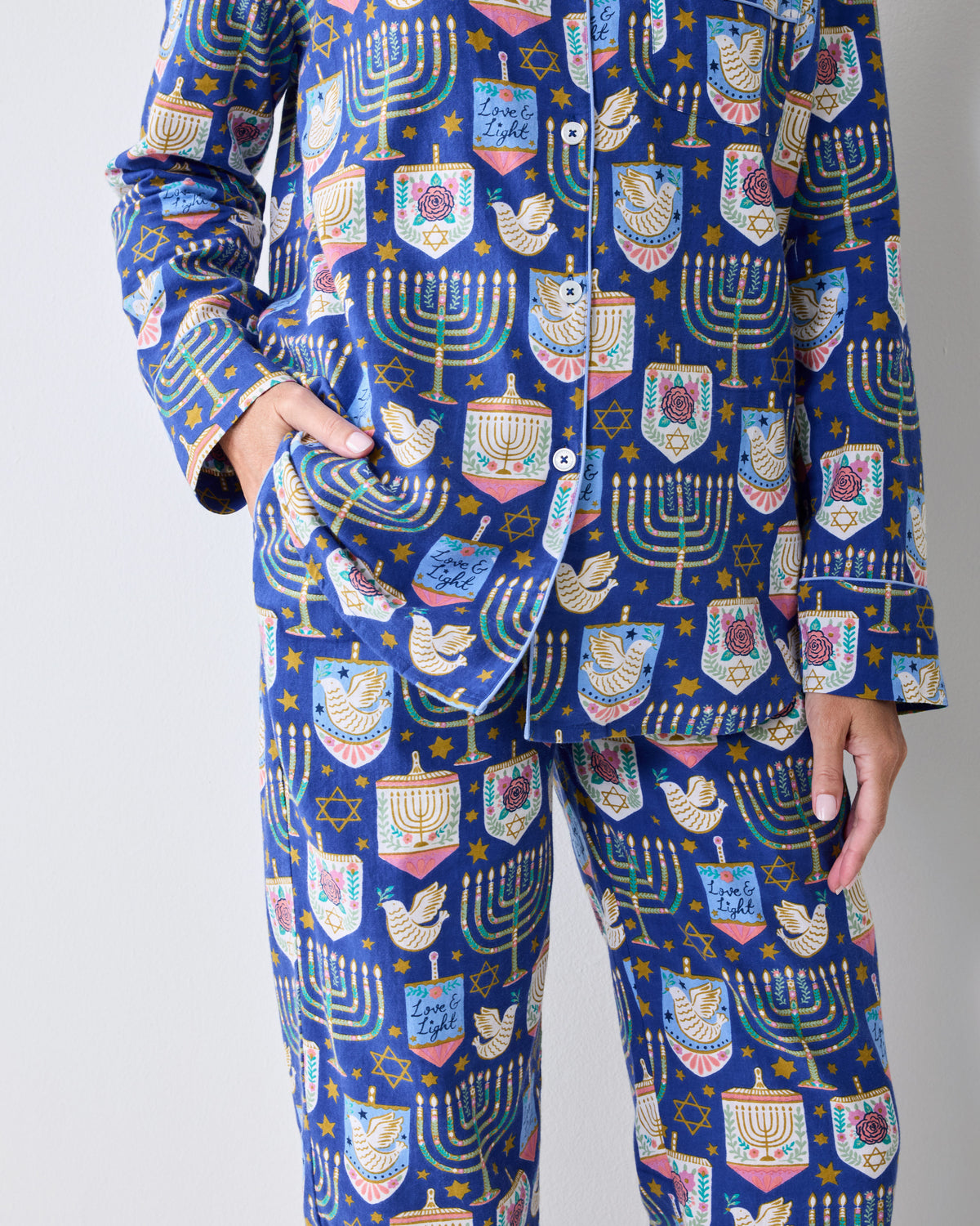 Close view of a blue long-sleeve pajama set with a Hanukkah print of menorahs, stars, dreidels, and other festive motifs.