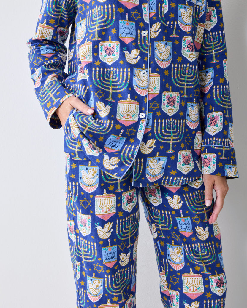 Close view of a blue long-sleeve pajama set with a Hanukkah print of menorahs, stars, dreidels, and other festive motifs.