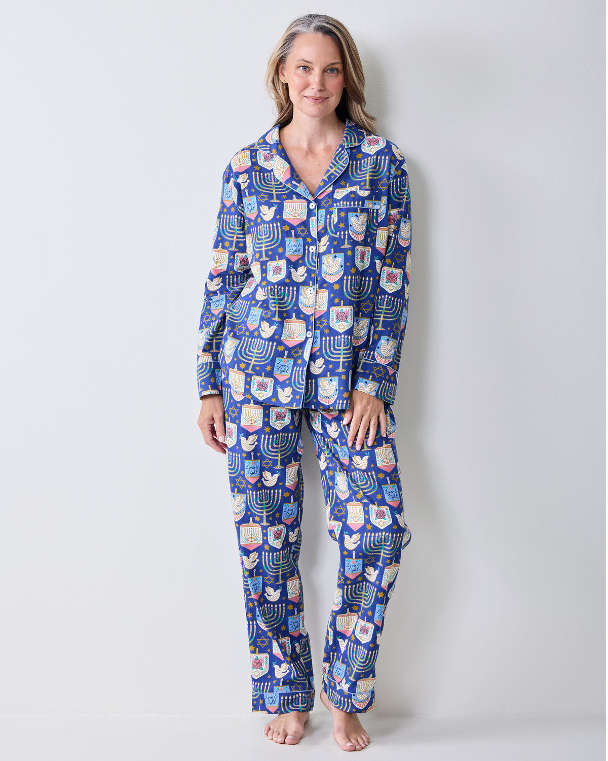 Full front view of a person wearing a blue long-sleeve collared pajama top with matching pants and a Hanukkah print.