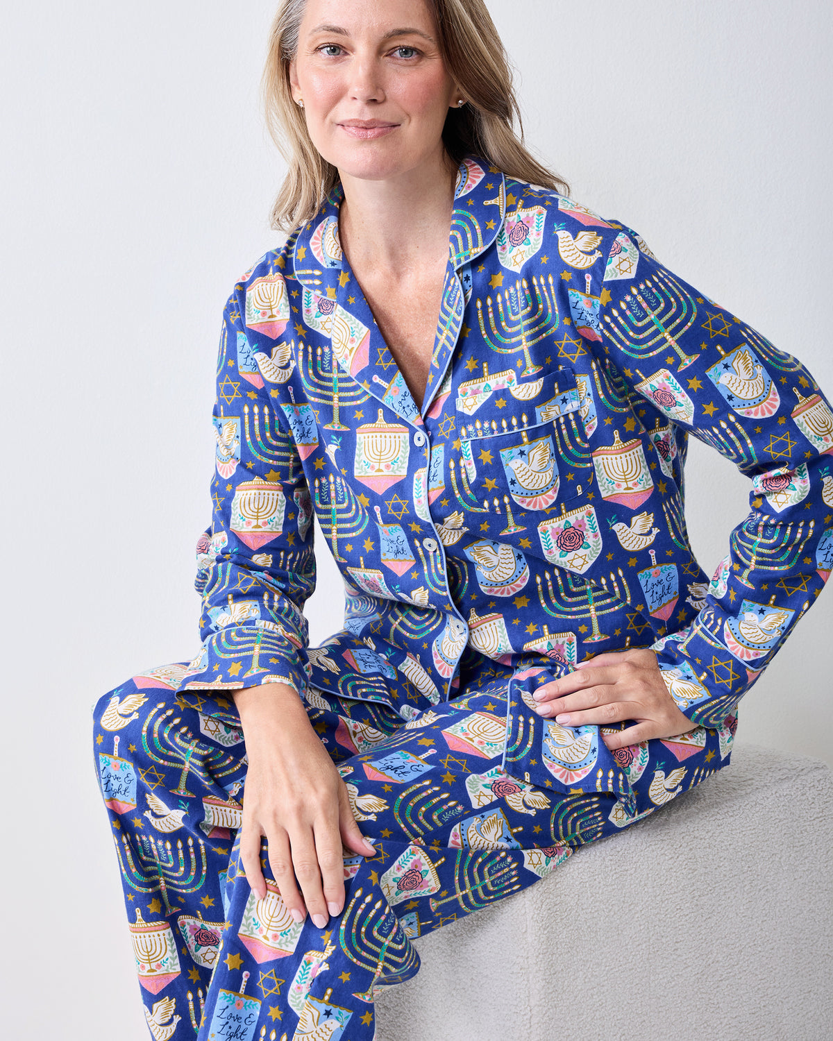 Front view of a person wearing a blue long-sleeve pajama set with a Hanukkah print, including a collared button-front top and matching pants.
