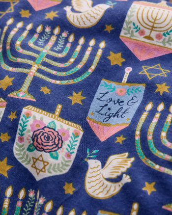 Close-up of the blue Love & Light pajama print featuring menorahs, stars, doves, floral motifs, and a label reading Love & Light.