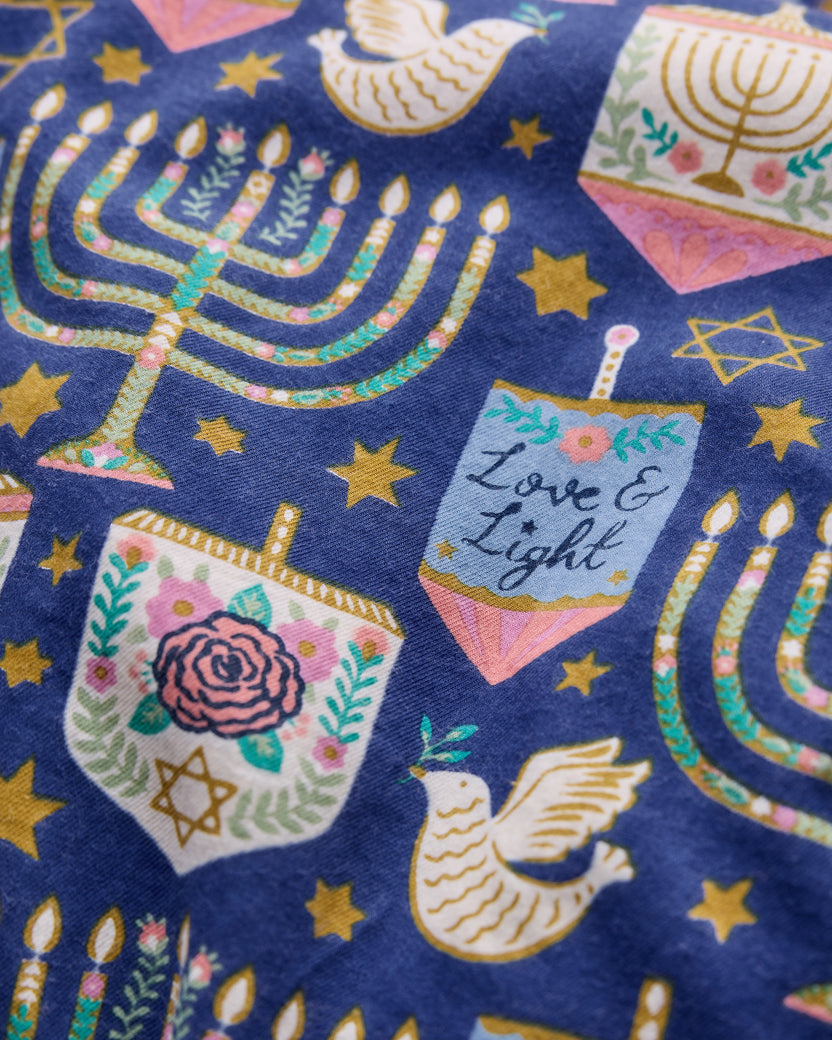 Close-up of the blue Love & Light pajama print featuring menorahs, stars, doves, floral motifs, and a label reading Love & Light.