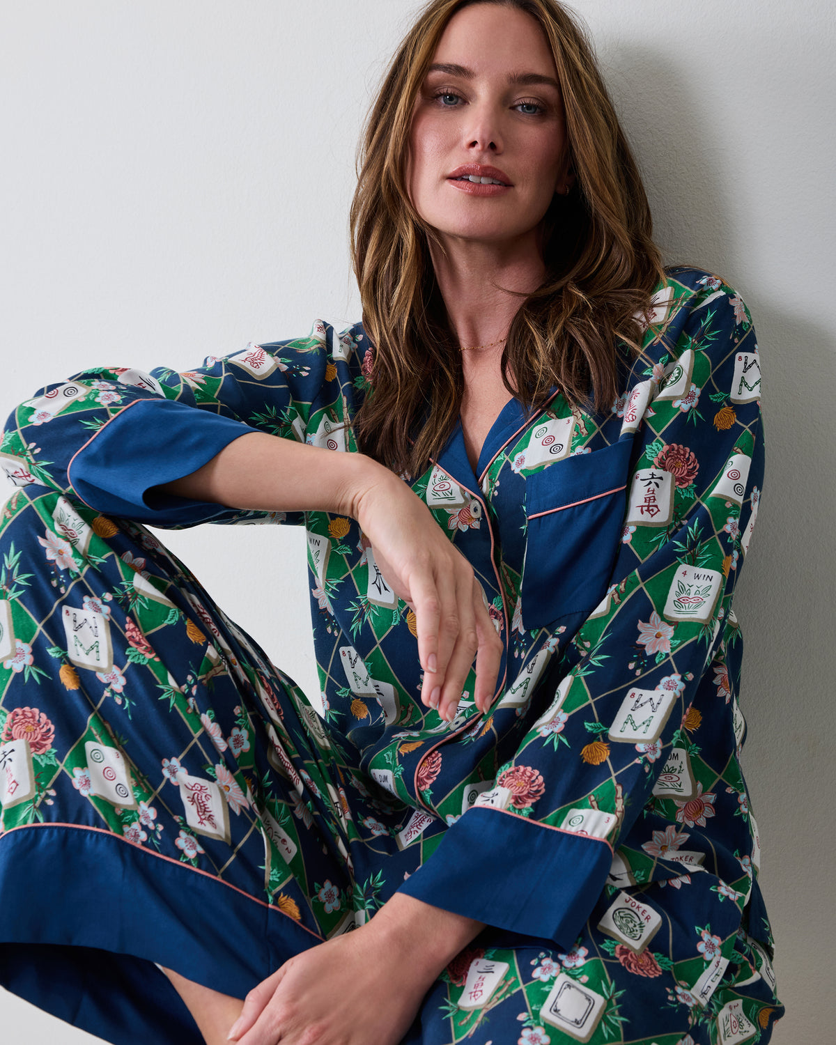 Seated front view of a person wearing the Mahj Garden Wintergreen Eco Satin Soho pajama set, showing the patterned button-front top and wide-leg pants.