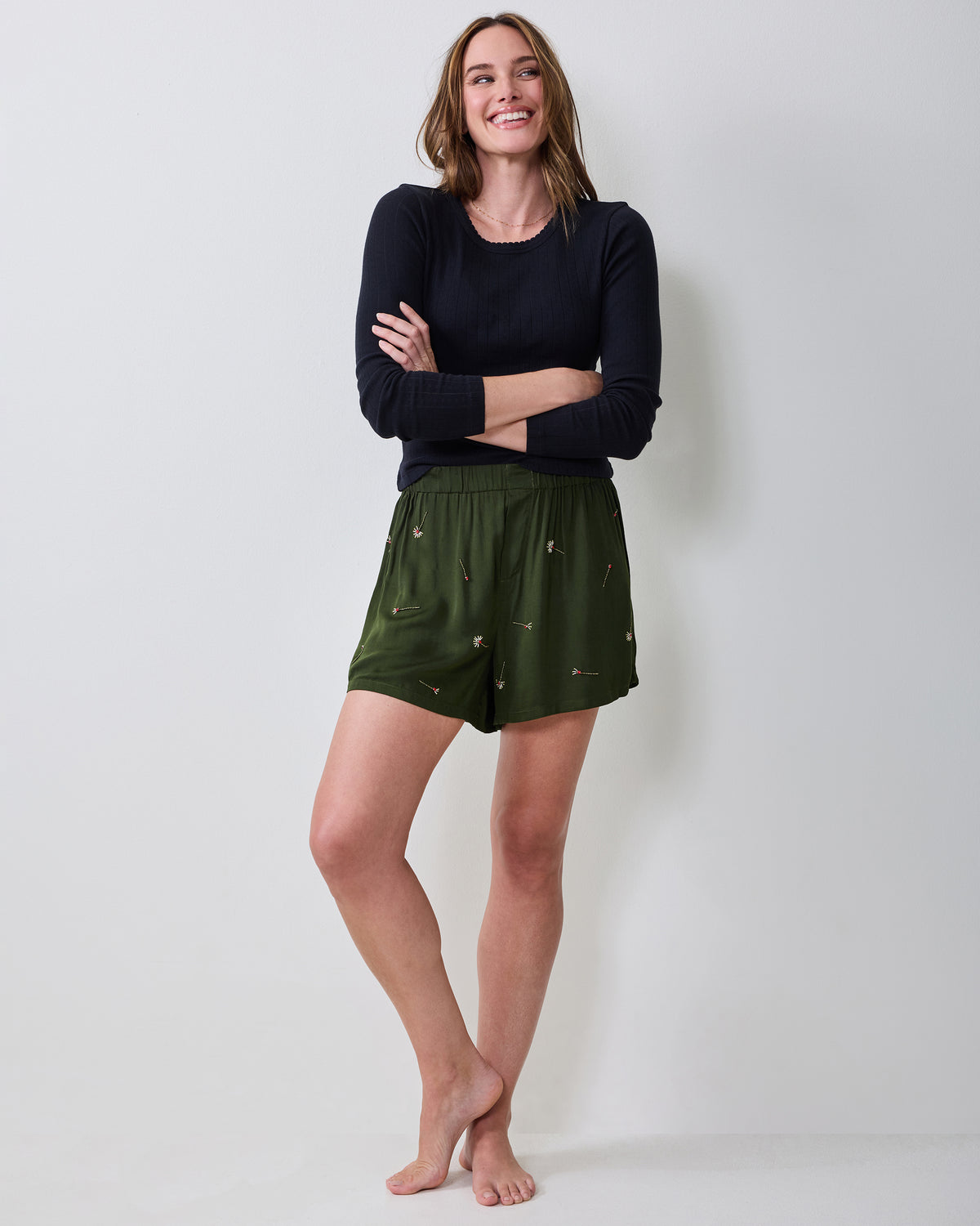 Model wearing olive embroidered boxer shorts with a black long-sleeve top.