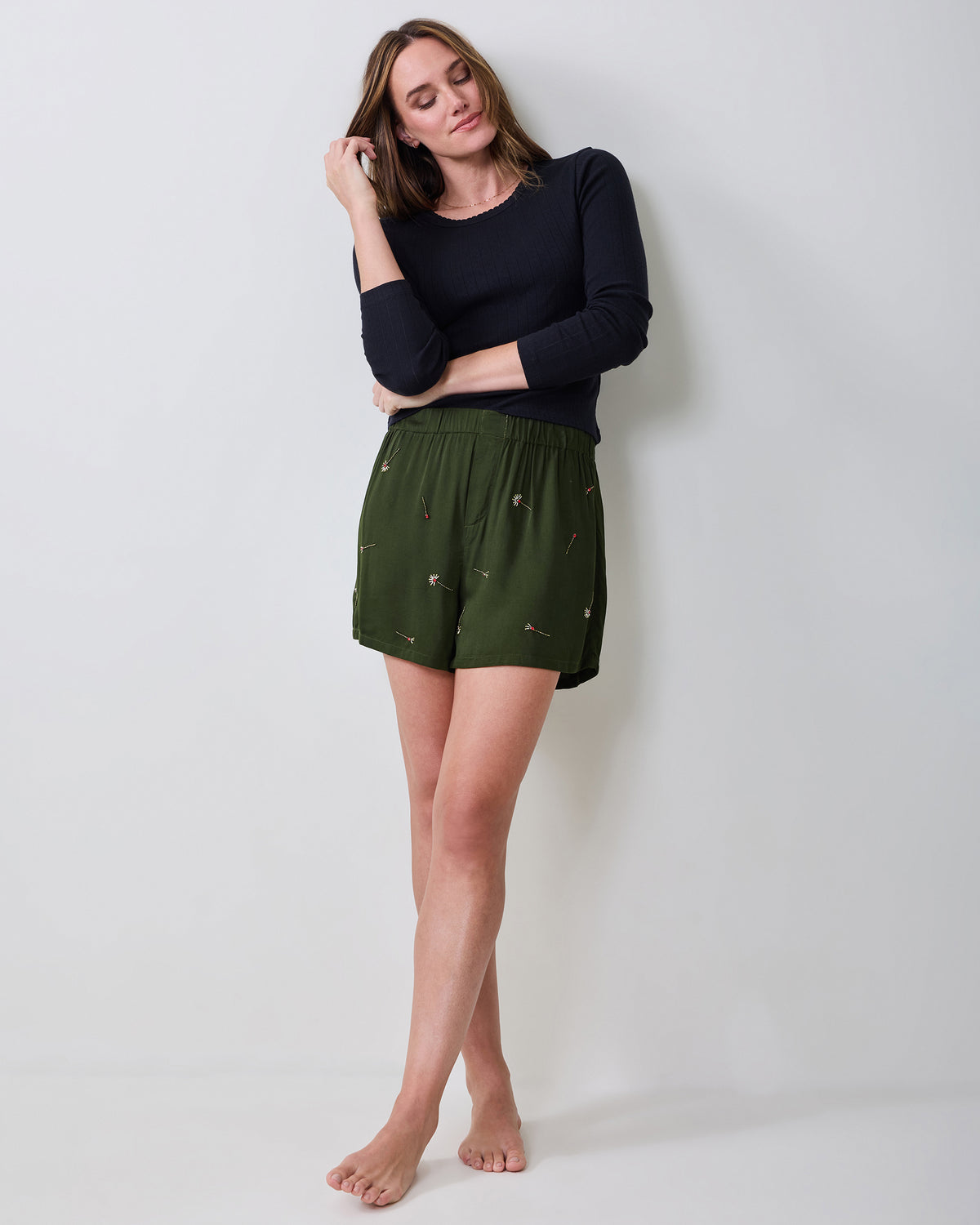 Full-length view of a model wearing olive embroidered boxer shorts with a black long-sleeve top.