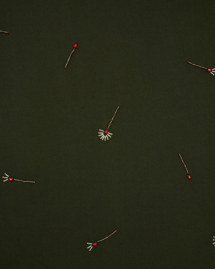 Close-up of the olive dress fabric with scattered embroidered match motifs and red bead details.