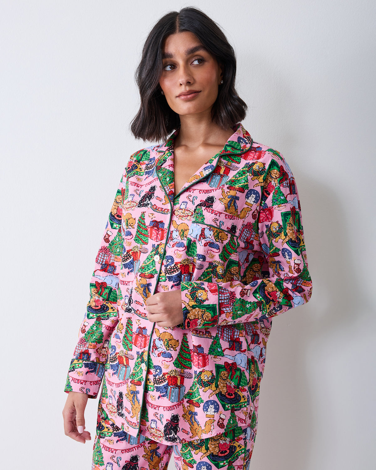 Three-quarter front view of a person wearing the candy pink long pajama set with a collared button-front top and matching Christmas cat print.