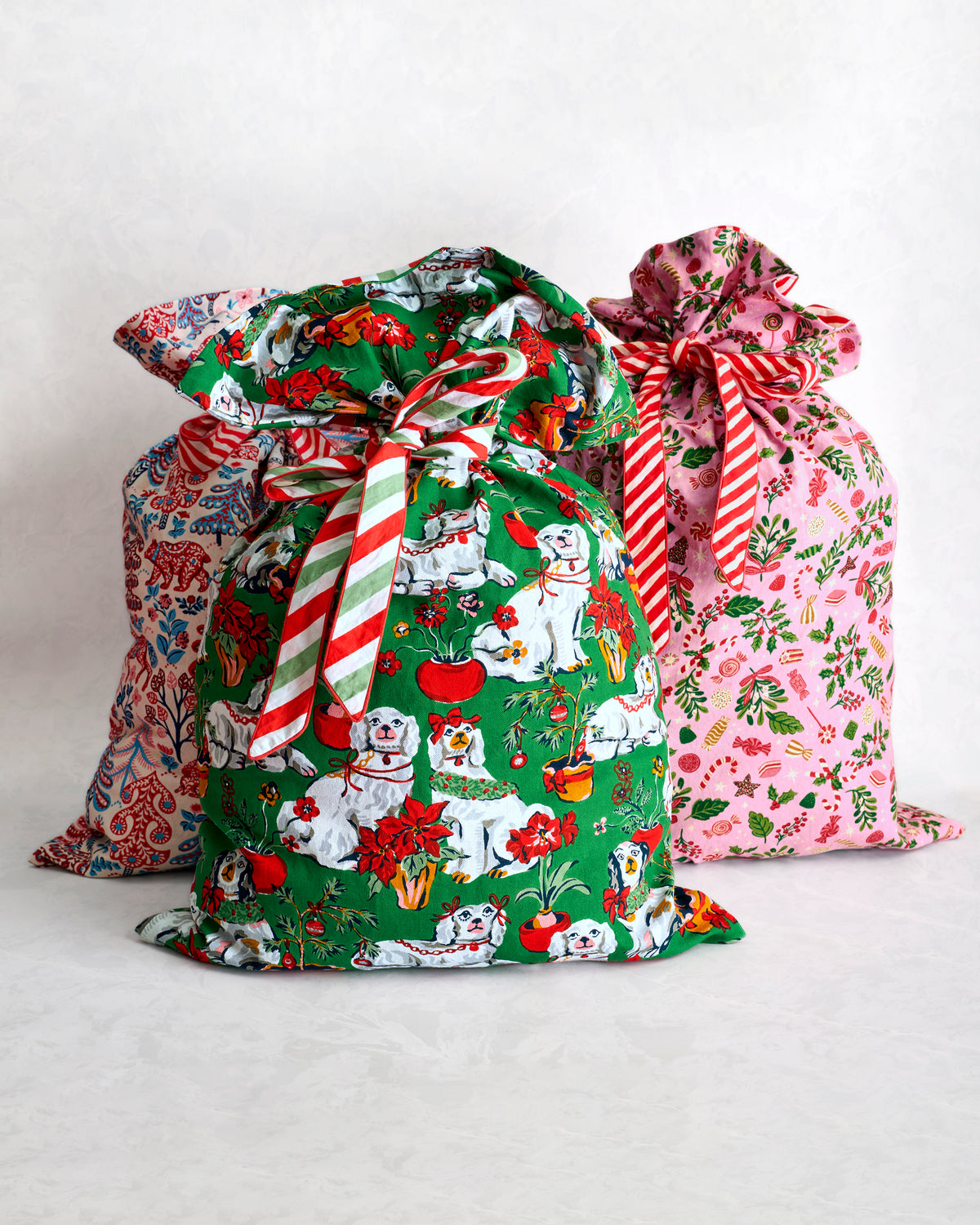 Three tied gift sacks in green, blue, and pink patterned designs, including a foreground sack with illustrated dogs and flowers.