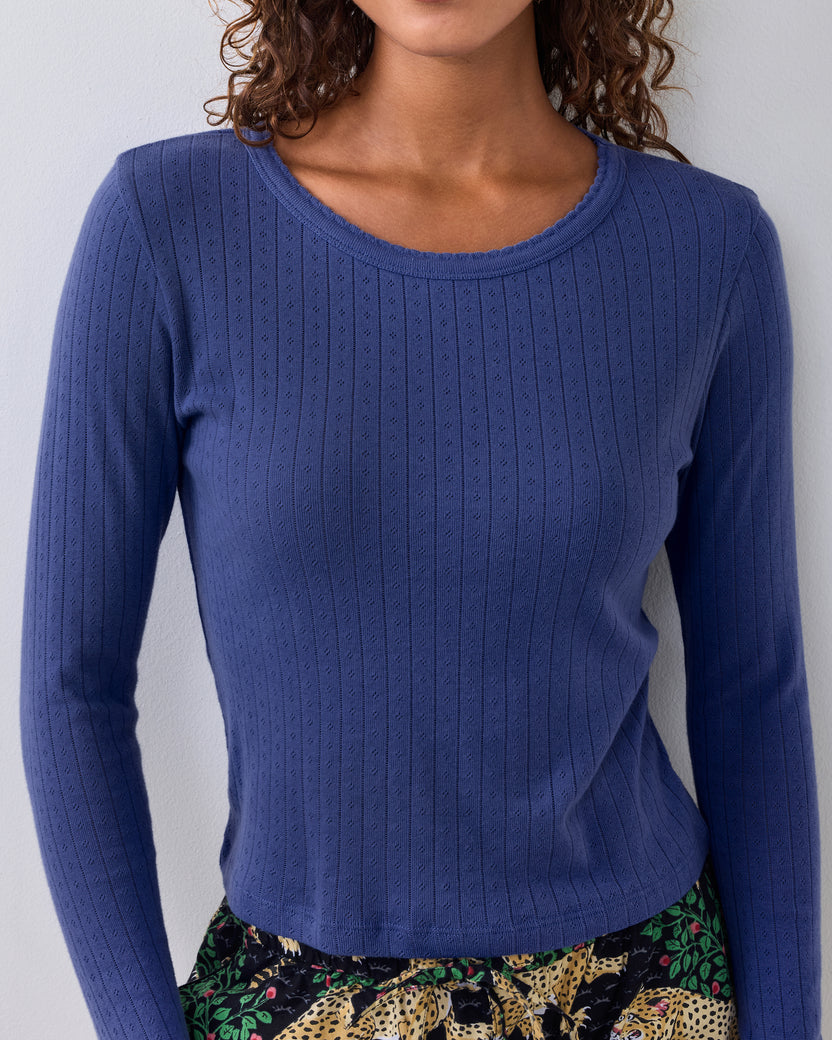 Blue long-sleeve pointelle top with a scalloped neckline, shown on a person with patterned pajama pants visible below.