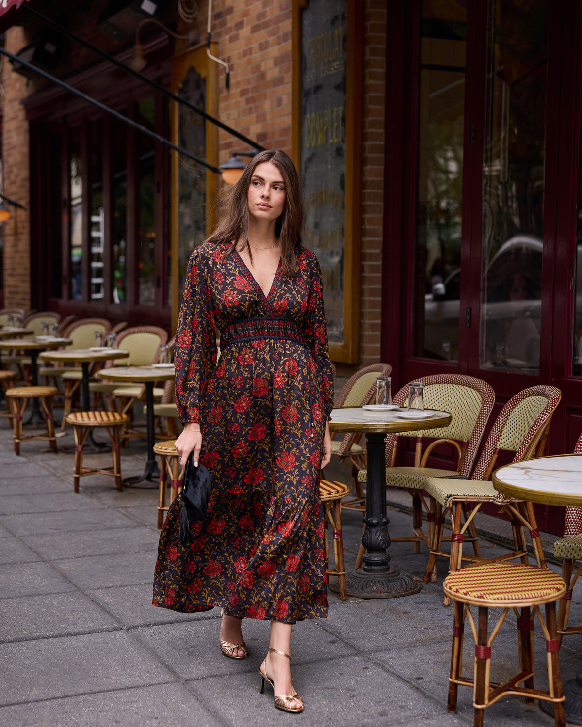 Full-length view of a person wearing a dark floral dress and sandals on a café sidewalk.