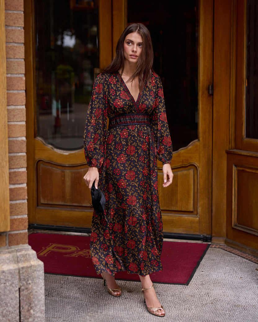 Person wearing the Linnia dress, a long-sleeved V-neck floral-print dress, standing in a doorway.