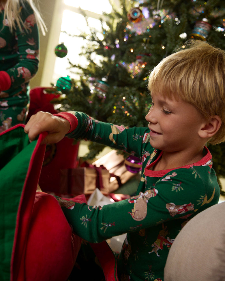 Child wearing the green Mistletoe Kiss long pajama set beside a decorated Christmas tree and gifts.