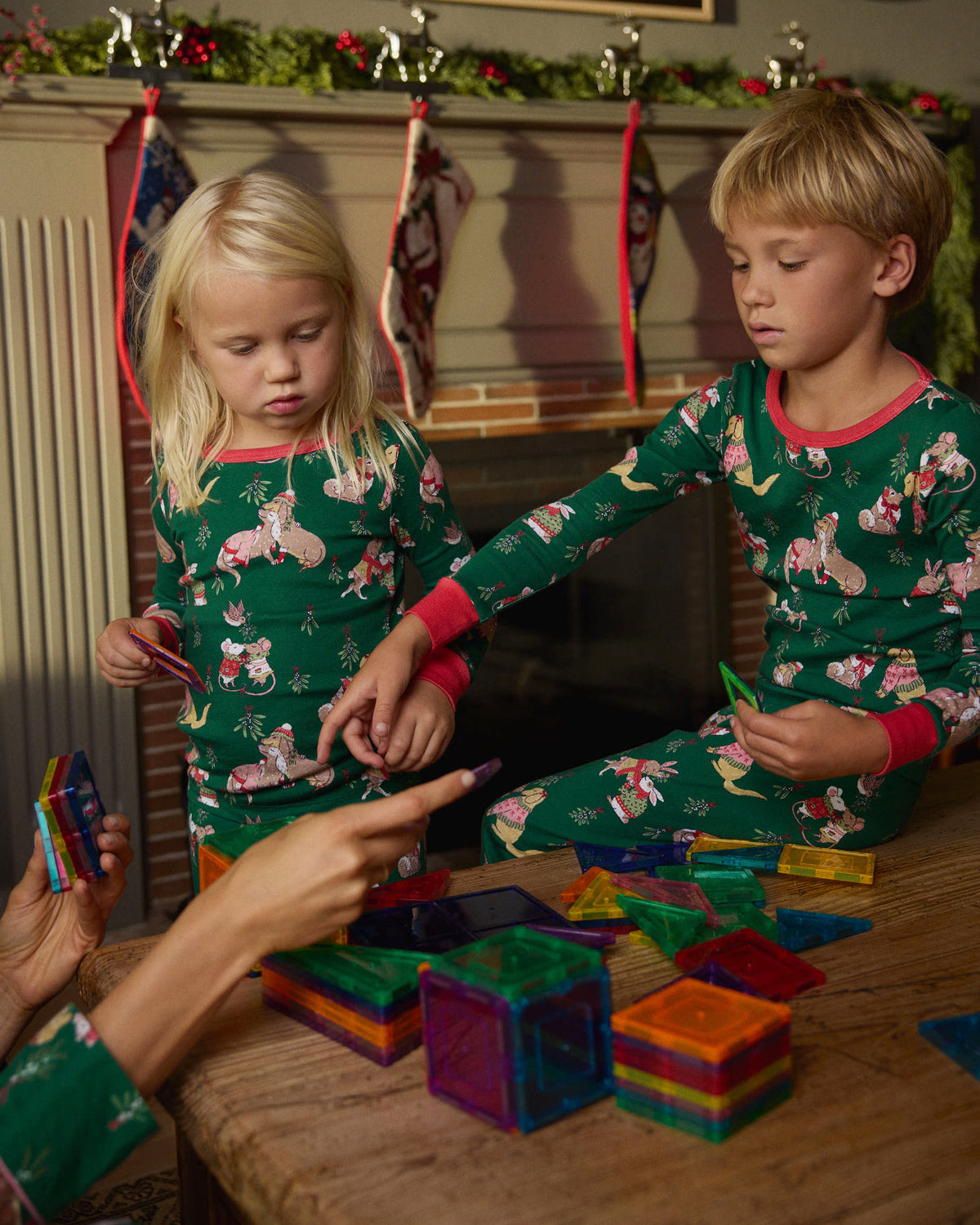 Two children wearing green Mistletoe Kiss long pajama sets while playing with colorful magnetic tiles.