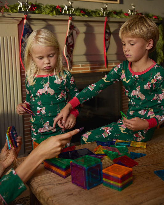 Two children wearing green Mistletoe Kiss long pajama sets while playing with colorful magnetic tiles.