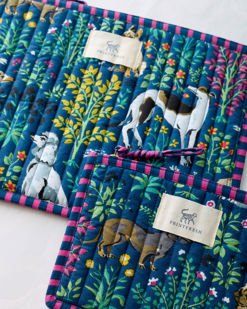 Close view of the indigo Must Love Dogs pouch duo showing dog illustrations, botanical motifs, labels, and striped trim.