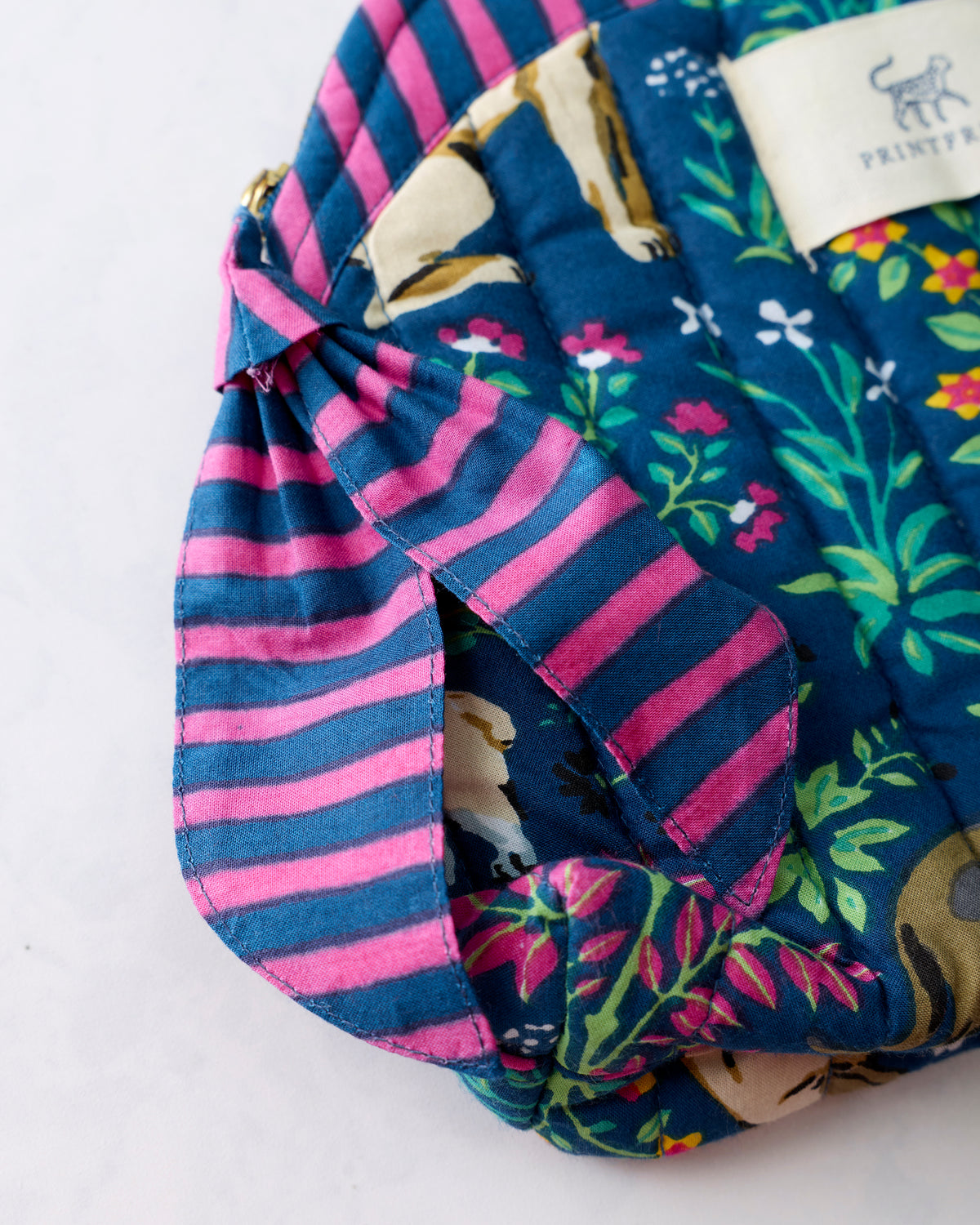 Close-up of the indigo quilted makeup bag showing its pink-and-blue striped trim, colorful floral and dog print, and Printfresh label.