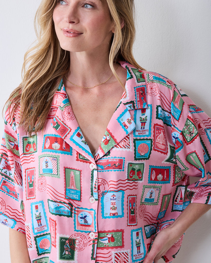 Close view of a person wearing the pink Nautical Stamps pajama top with a notched collar, buttons, and colorful postage-stamp print.