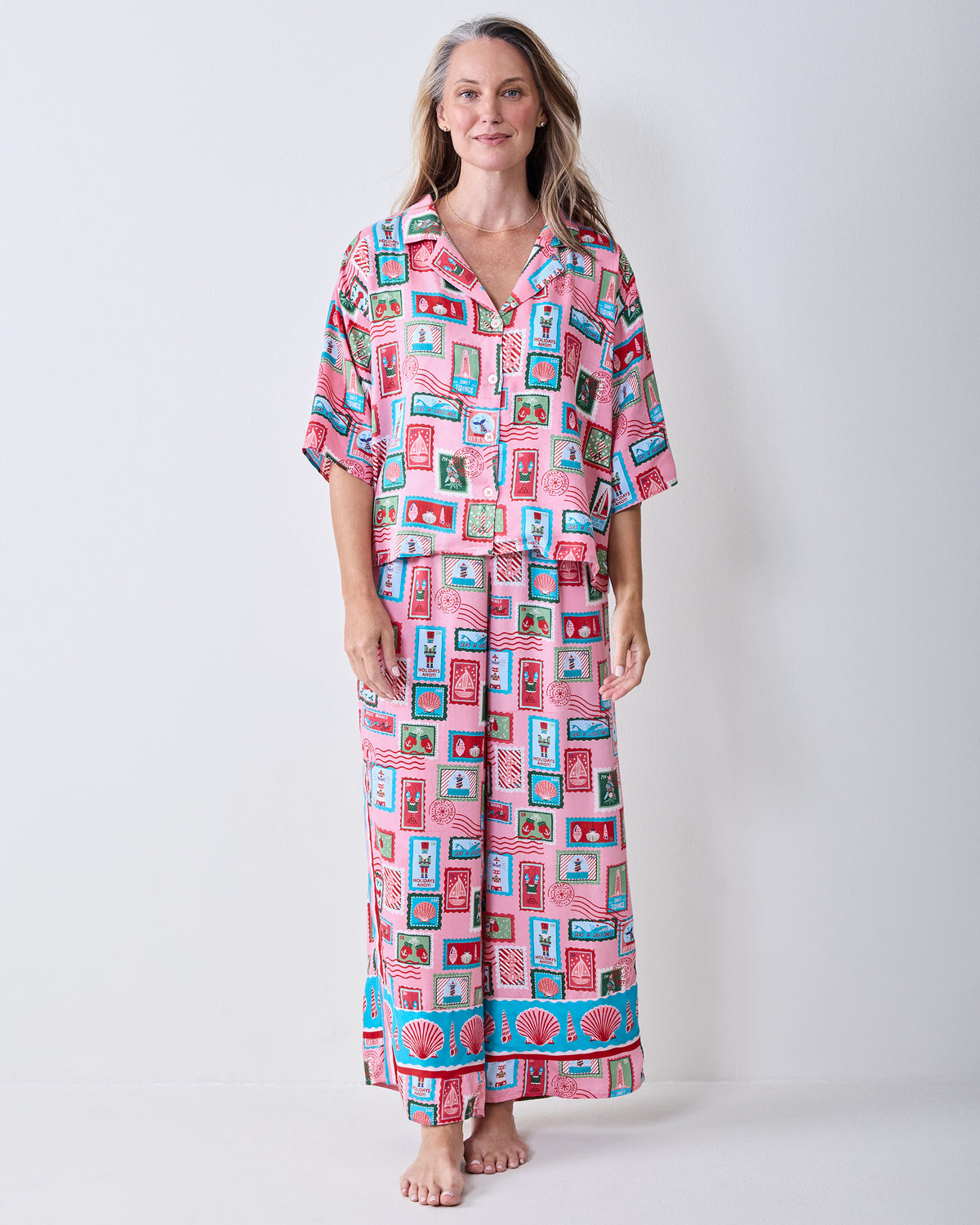 Full-length front view of a person wearing the pink Nautical Stamps long pajama set with a button-front top and straight-leg pants.