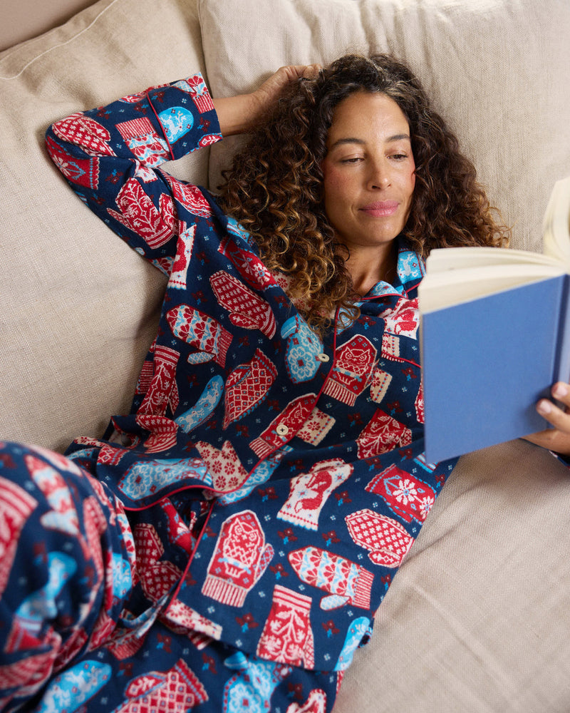 Person reclining on a bed wearing the Nordic Mittens Viking Blue long pajama set and holding a blue book.