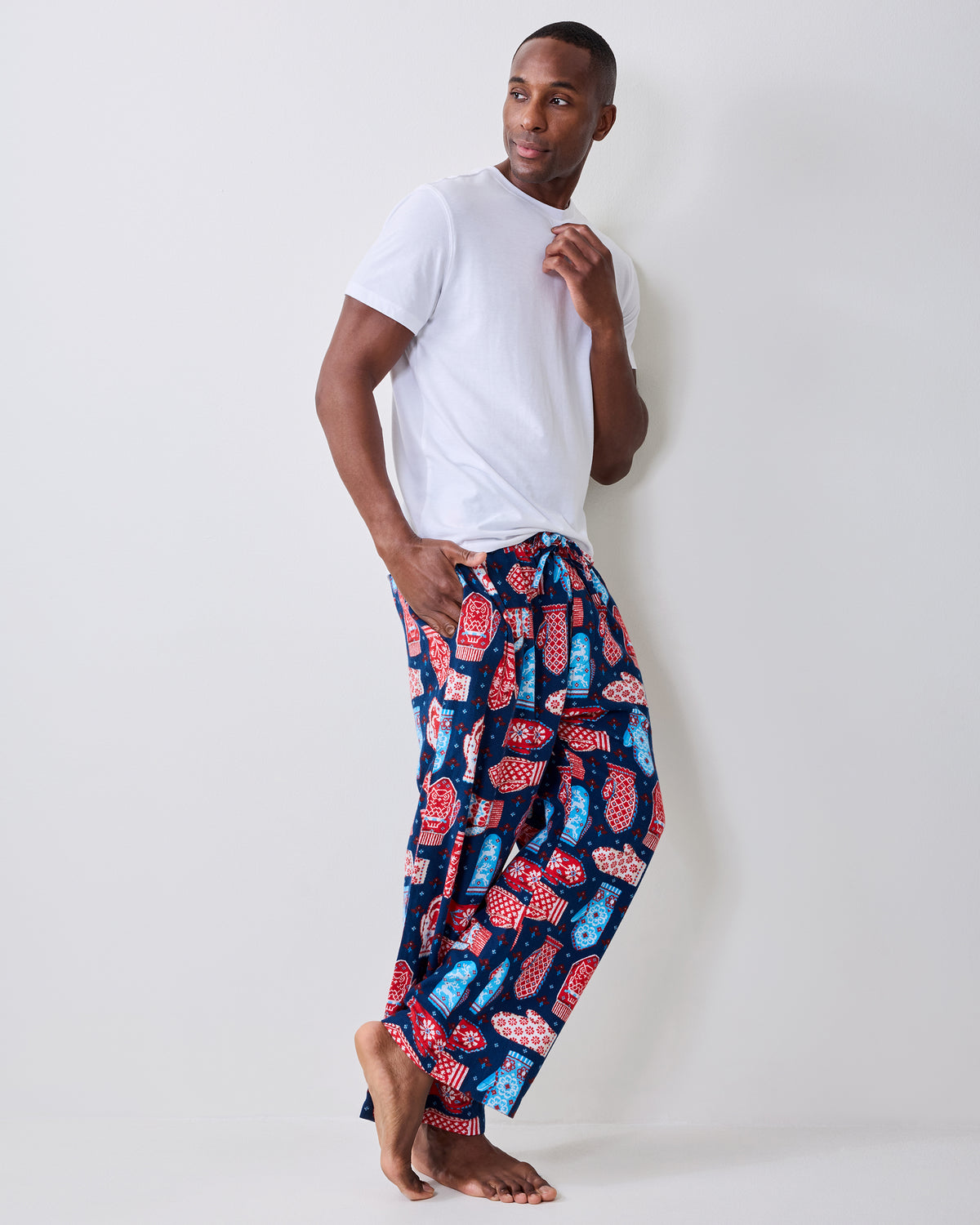 Side view of blue flannel men's pajama pants with a red, white, and light blue mitten print, worn with a white T-shirt.