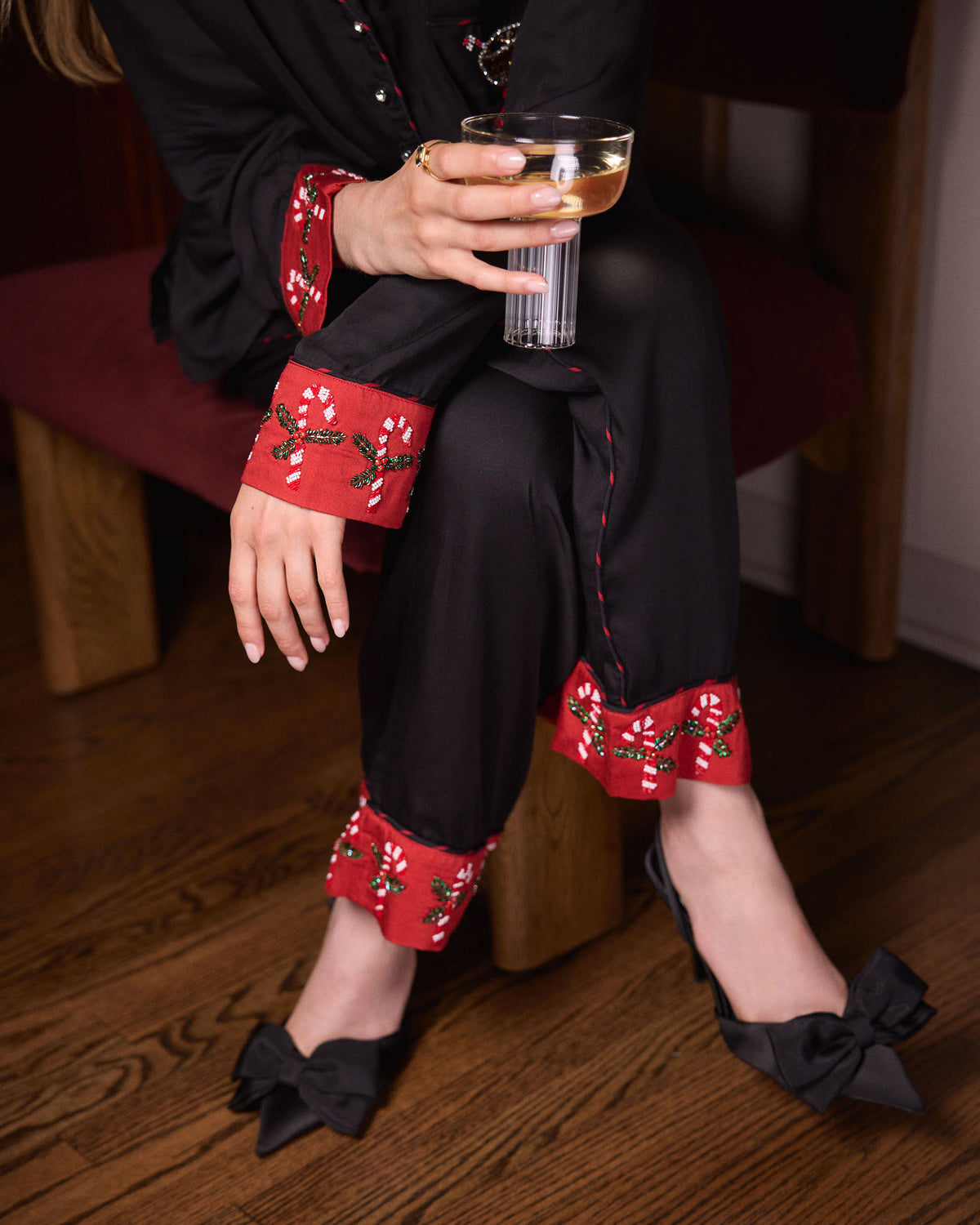 Close-up of the Onyx Peppermint Martini pajama set showing red embroidered cuffs on the sleeves and pant legs while holding a cocktail glass.