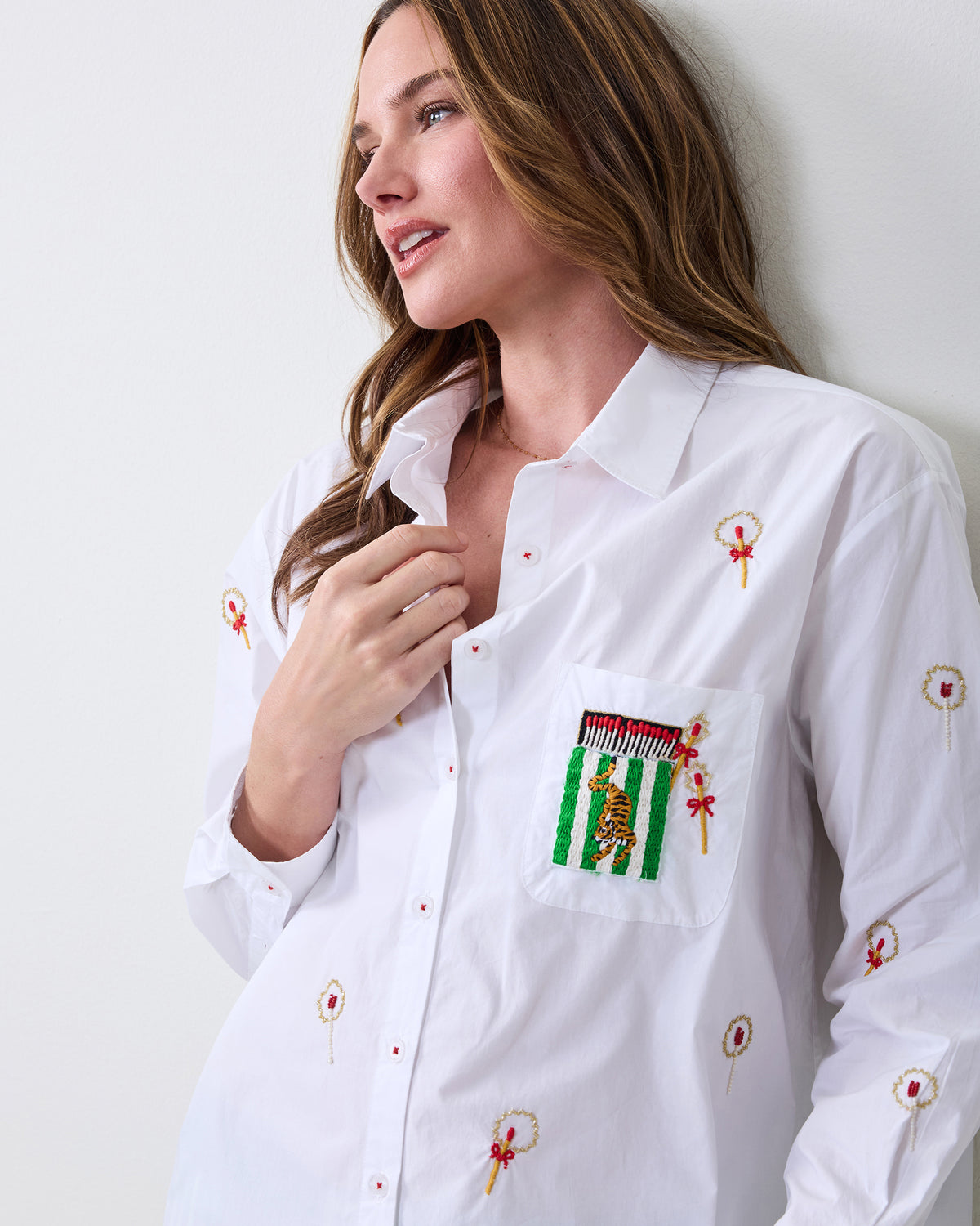 Close-up of the white button-down shirt showing embroidered matchstick motifs and a chest pocket with a striped tiger design.