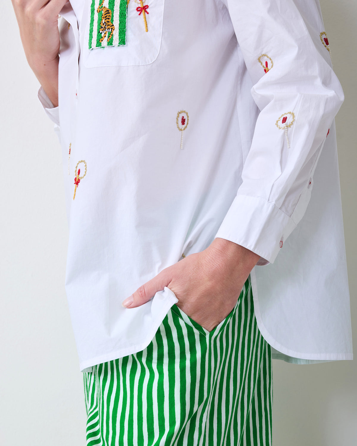 Close-up of the white embroidered shirt over green-and-white striped pants, with a hand in the pants pocket.