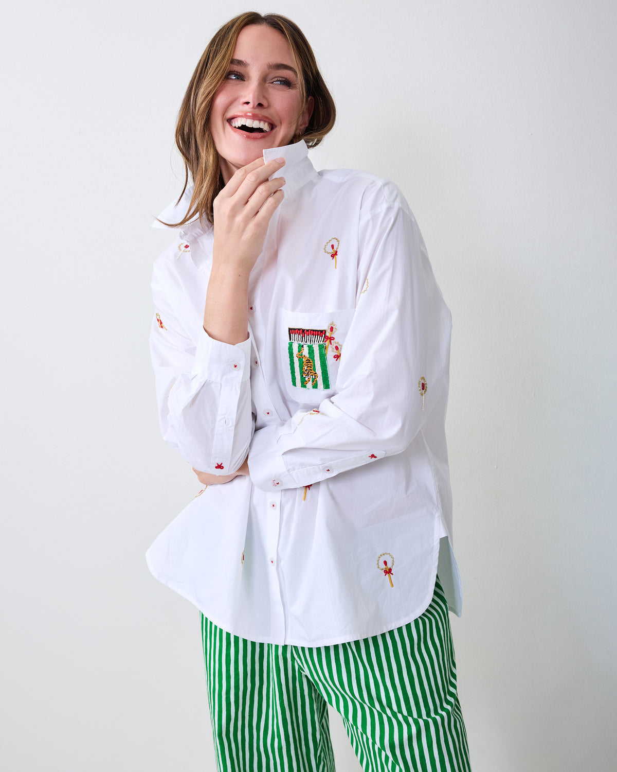 Model wearing a white embroidered button-down shirt with green-and-white striped pajama pants, holding the shirt collar.